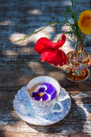 Porcelain cup of tea and beautiful spring flowers in vase on a wooden table in the garden. Summer party. Selective focusの写真素材