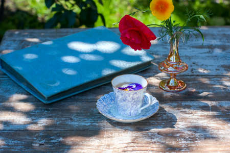 Porcelain cup of tea and beautiful spring flowers in vase on a wooden table in the garden. Summer party. Selective focusの写真素材