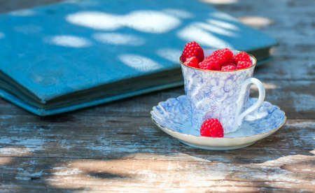 Fresh ripe raspberries and an old porcelain cup with a saucer on a wooden table in the garden. Selective focusの写真素材
