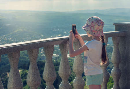 A little girl is taking pictures with a mobile phone camera in nature, in the mountains.の写真素材