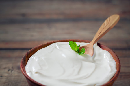 Greek yogurt in a wooden bowl on a rustic wooden table.