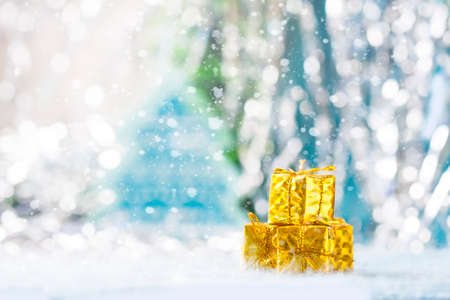 Golden gift box under the Christmas tree on a blue background. Snowing. Selective focusの写真素材
