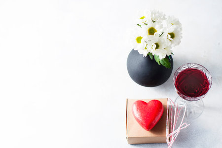 White daisies in a clay pitcher, a glass of wine and two hearts. The 14th of February.