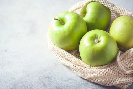 Organic green apples in reusable cotton net bag on wooden table. Eco-package, zero waste concept. Selective focus.の写真素材