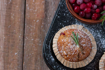 Fresh homemade Cranberry muffins in baking form on wooden table with Christmas decoration. Muffins in eco-friendly recyclable paper packaging.の写真素材