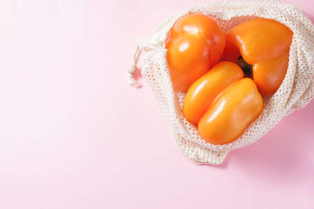 Organic orange bell pepper in reusable cotton net bag on wooden table. Eco-package, zero waste concept.の写真素材
