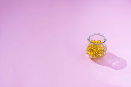 Capsules Vitamin D and Omega-3 tablets for a healthy diet on a pink background. Fish oil based...