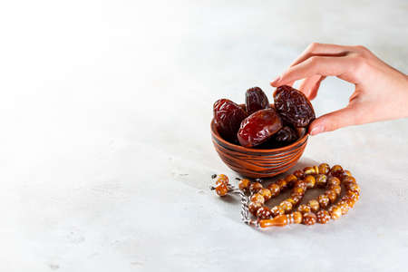Plate with dates, decorative arabic lantern and rosary on a light background. Holy month of Ramadan concept. Children's hand reaches for a plate with dates. Selective focus, copy spacyの写真素材