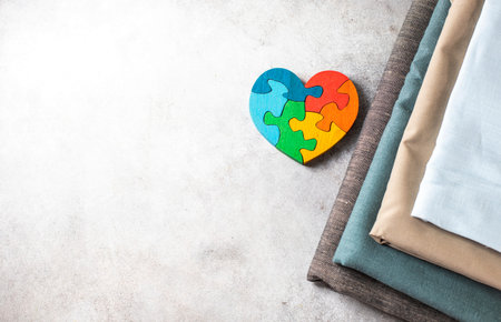 Natural fabrics for children's clothing and a wooden puzzle toy in the shape of a heart. Neutral baby clothes. Top view, flat lay.の写真素材