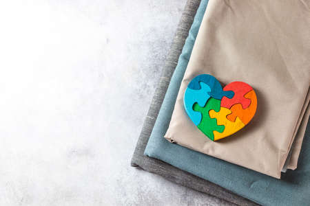 Natural fabrics for children's clothing and a wooden puzzle toy in the shape of a heart. Neutral baby clothes. Top view, flat lay.の写真素材