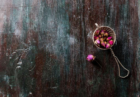 Buds of tea rose for tea in a vintage strainer on a on a dark wooden background. Selective focus, copy space. Top view.の写真素材