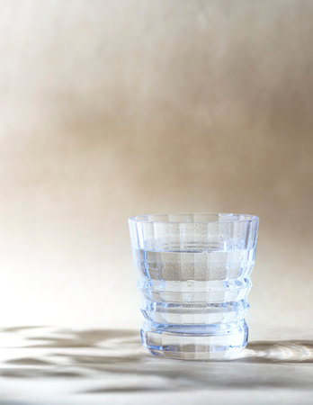 Water in a crystal glass on a beige background. Copy space, selective focus