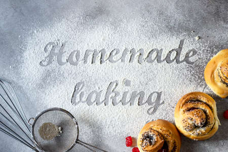The inscription on the flour Homemade baking. Homemade buns with poppy seeds, tools and baking products on a light background. Making pastry concept.の写真素材