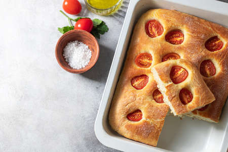 Italian bread focaccia with tomatoes and sea salt on grey concrete background. Homemade baking. Top view, copy space.の写真素材