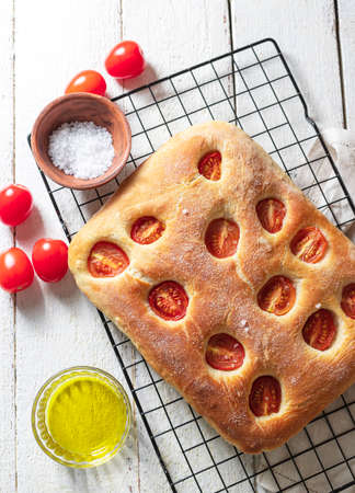Italian bread focaccia with tomatoes and sea salt on a white wooden background. Homemade baking. Top view, copy space.の写真素材