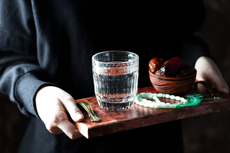 A female hand holds a tray with dates, and water and a rosary - hthe things used to break the fast...