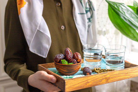 A female hand holds a tray with dates, and water and a rosary - hthe things used to break the fast...