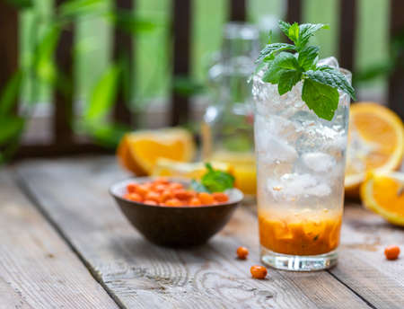 Sea buckthorn ice lemonade with oranges. Fruits and berries outdoors on a wooden table. Detox drinks. Selective focus, copy spaceの写真素材