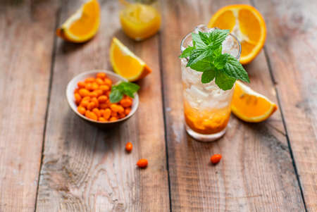 Sea buckthorn ice lemonade with oranges. Fruits and berries outdoors on a wooden table. Detox drinks.の写真素材