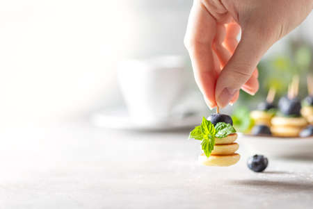 Trendy food - mini pancakes with blueberries and mint in female hands on a light concrete background.の写真素材