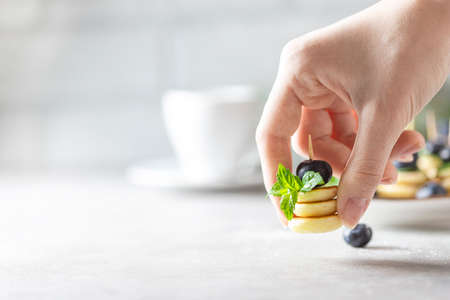 Trendy food - mini pancakes with blueberries and mint in female hands on a light concrete background.の写真素材