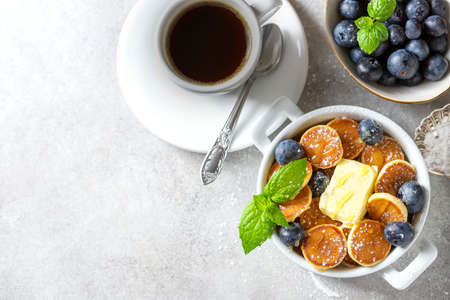Bowl with tiny pancake cereal on a light concrete background. Trendy food. Mini cereal pancakes with butter, honey and blueberries. Copy spaceの写真素材