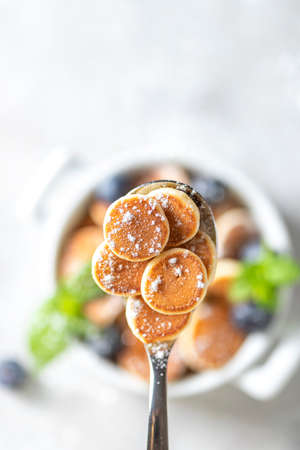 Pancake porridge. Mini pancakes on a spoon on a light concrete background. Trendy food mini pancakes. Copy space, selective focusの写真素材