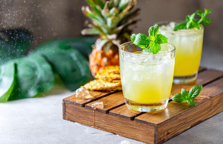 Freshly squeezed pineapple juice with slices of pineapple on a light gray concrete background. Concept of summer healthy fruit drink. Selective focus, copy space.の写真素材