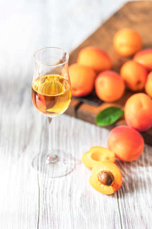Apricot liqueur in shot glass and fresh apricots on a light wooden table. Selective focusの写真素材