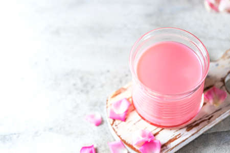Ayurvedic rose moon milk. A trendy relaxing form of drink before bed. Milk with rose petals on a light concrete background. Selective focus, copy space. View from aboveの写真素材