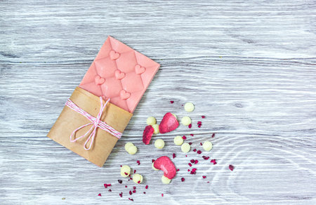 Pink chocolate whole bar decorated with slices of fruit nuts and slices against gray background....