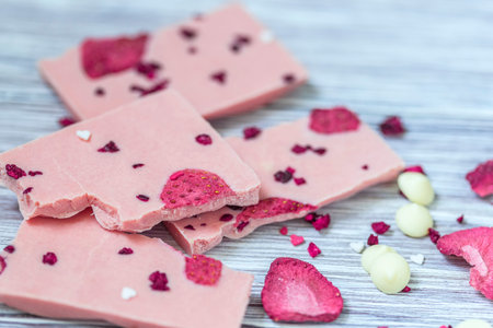 Pink chocolate whole bar decorated with slices of fruit nuts and slices against gray background....