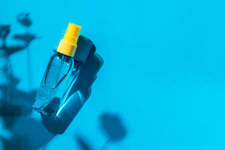 Cosmetic spray bottle blue and yellow with transparent liquid on a blue background. Spa cosmetics. Natural skincare. Copy space, top view.の写真素材