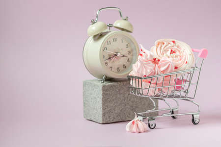 Pink mezies in a small shopping cart and an alarm clock on a pink background. Creative concept food health diet. Selective focus, copy spaceの写真素材