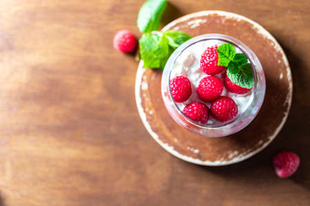 Homemade cottage cheese with fresh raspberries in a glass glass on a rustic wooden background. Dietary breakfast. Russian cottage cheese with berry and mint. Selective focus, copy space.の写真素材
