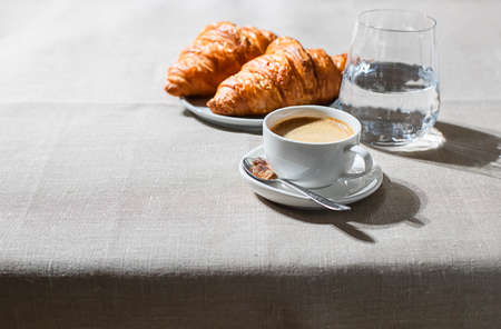 Croissants and cup of coffee in the morning light, sunlight shadow, on a linen fabric. Morning breakfast concept.の写真素材