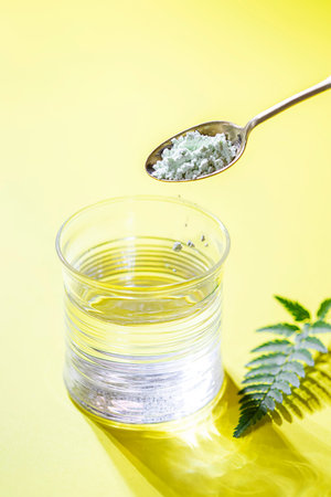 A glass of water, collagen powder on a bright yellow background. Healthy lifestyle concept.