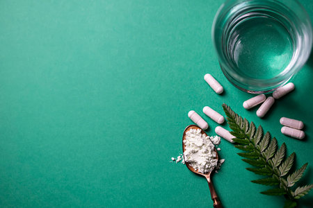 Glass of water, powder and capsules with collagen on a green background. Natural beauty and health...