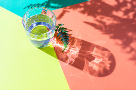 Glass of clear transparent water on a colorful background in natural light with harsh shadows.