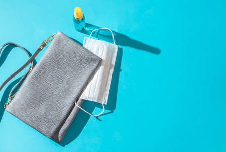 Leather woman bag out with face mask, sanitizer hand gel to protect from Coronavirus or COVID-19 on a blue background with sunlight shadow. Copy space, flat layの写真素材