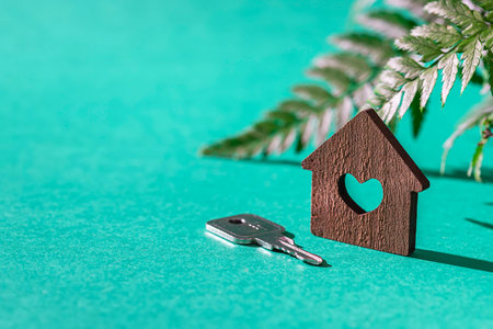 Miniature wooden house with a key on a green background. Dream house concept, real estate...