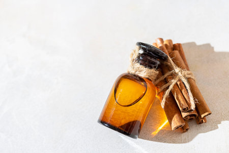 Cinnamon essential oil in a bottle and cinnamon sticks on a light concrete background. Spa concept. Selective focus.の写真素材