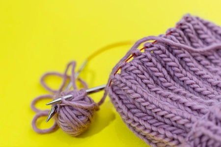 The cap is connected by circular spokes on the wire on a yellow background. Process of knitting....