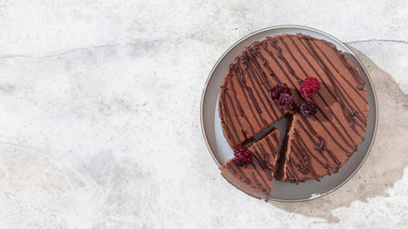 Classic chocolate cheesecake on light gray concrete background. Homemade baking. Vegan sugar gluten...