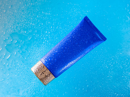 Cream cosmetic tube of blue color with a gold cap in clean transparent water with sunlight on a blue background. Natural organic cosmetology in a clean beautiful drop of water. Copy spaceの写真素材