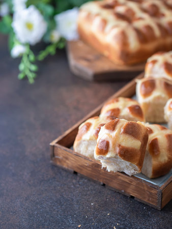 Homemade Hot Cross Buns on a wooden board on brown background. Traditional Easter food. Easter...