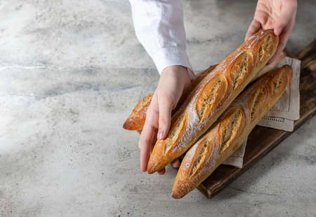 Female baker holds fresh baked French baguette. Homemade sourdough bread. Homemade food. Food preparation.の写真素材