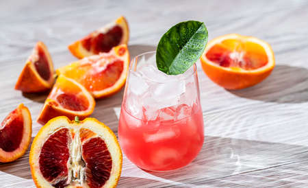 Red orange juice in a glass and oranges with sunlight and shadows. Cocktail from Sicilian oranges, selective focus. Long harsh shadows.の写真素材