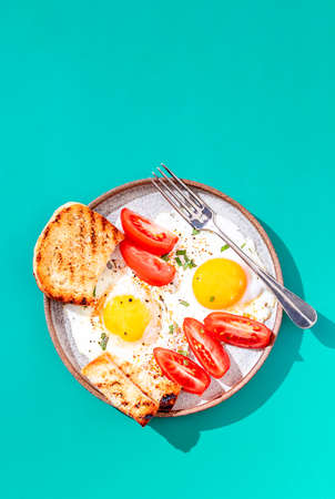 Two fried eggs with toast with avocado slicesand vegetables on colorful background. Breakfast concept. Healthy vegetarian food. Close up, copy spaceの写真素材