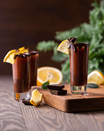 Cocktail in shot glass with chocolate, cream liqueur, fresh oranges on dark background. Homemade shot drinks party. Bar menu, recipes. Close up, selective focusの写真素材